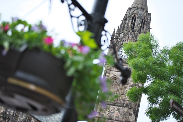 In the foreground is a hanging basket with flowers looking blurry, behind it, in focus is the tall clock tower of a church