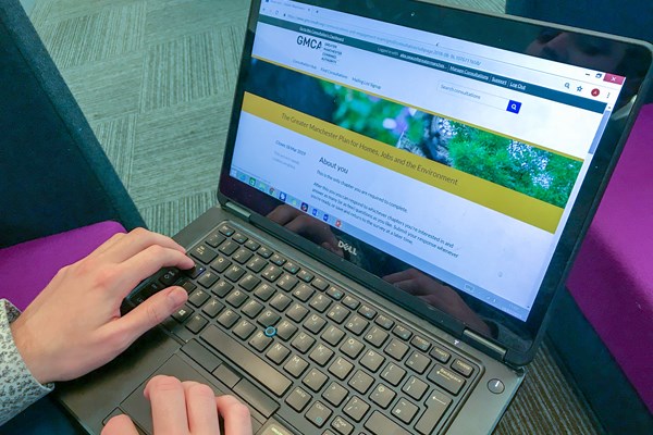 A person presumed to be looking at a web page on a laptop. Their two hands can be seen resting on the laptop keyboard with the screen showing a webpage that includes the words GMCA.