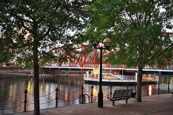 A view of a park bench beside water with a bridge in the background.