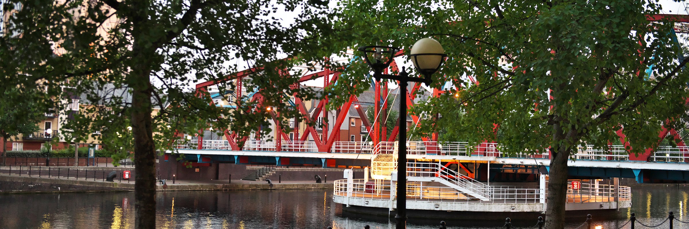 A view of a park bench beside water with a bridge in the background.