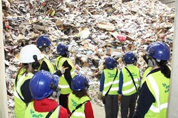 A group of school children stand in front of a large pile of paper and card in the tipping hall