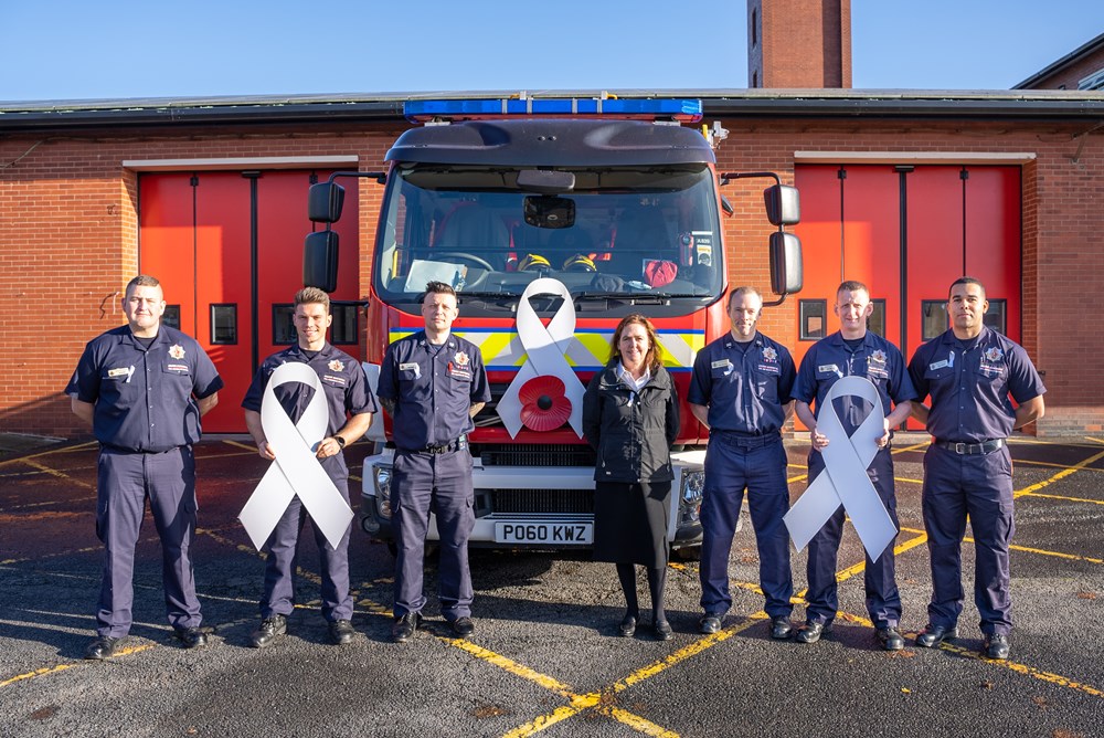 Firefighters from Greater Manchester Fire and Rescue Service stood outside Agrecroft community fire stations holding White Ribbons and stood in front of a fire engine with a large White Ribbon and poppy on it.