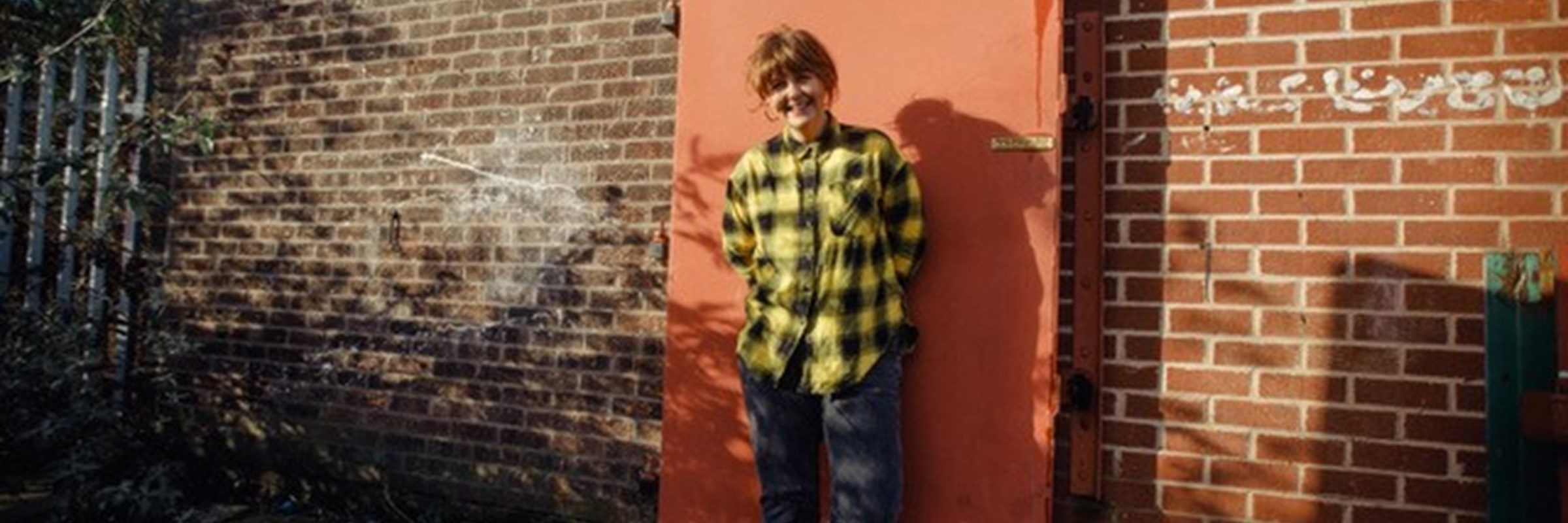 Photo of Test Card Girl stood in front of a red door on a brick building