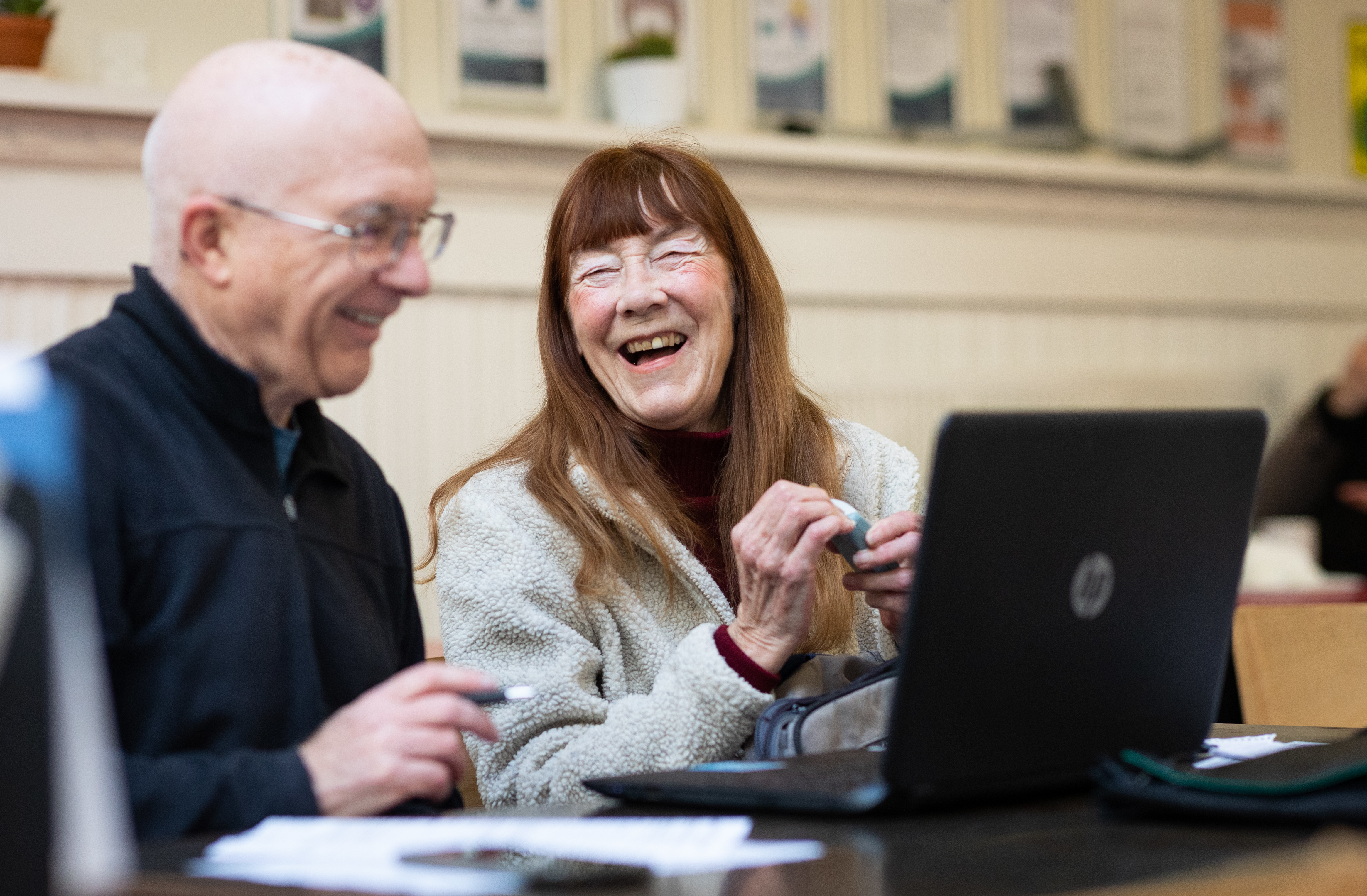 Two older people laughing, using computers
