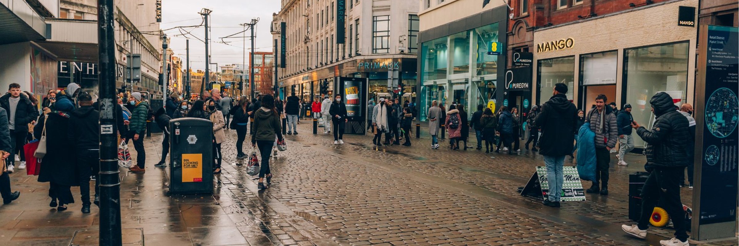 A busy city street  in Manchester with people walking and standing on the pavement