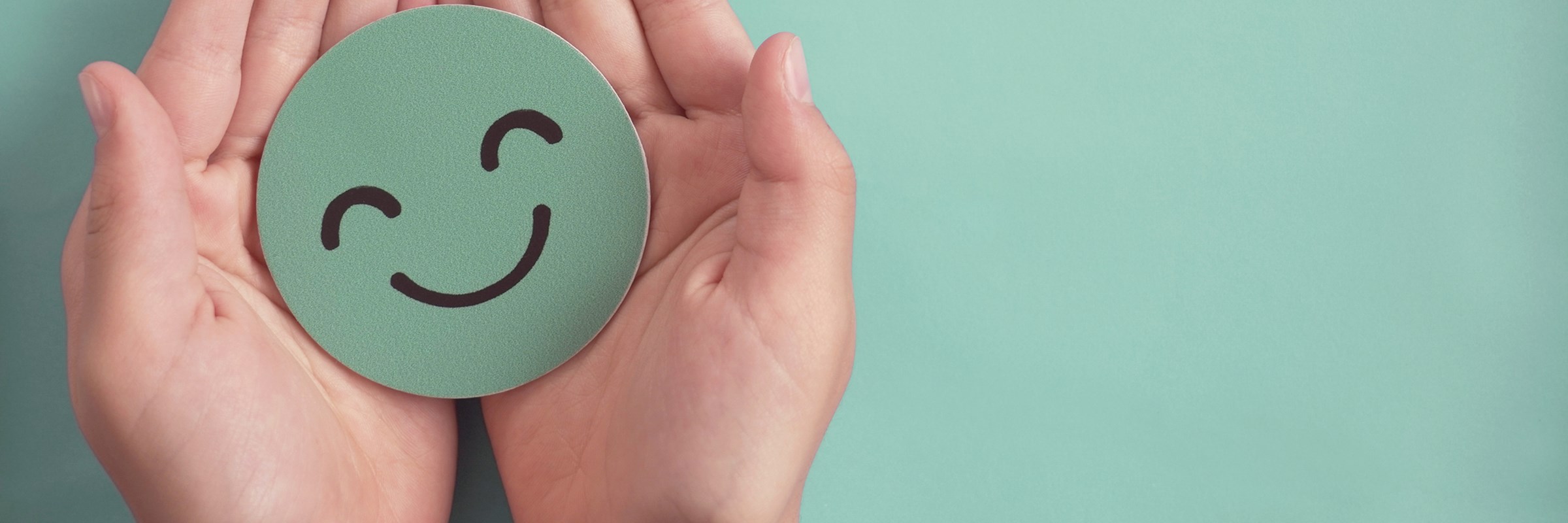 Two cupped hands holding a green circle piece of card with a smiley face drawn on.