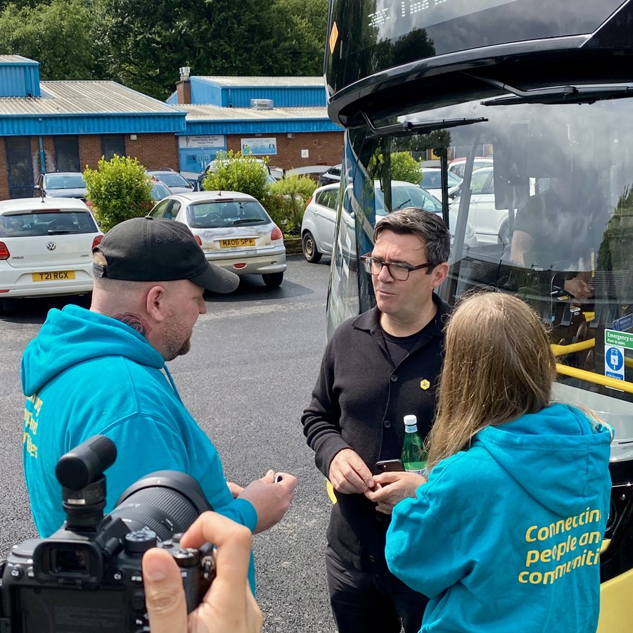 Andy Burnham stood in front of a Bee Network bus talking to two members of a community group